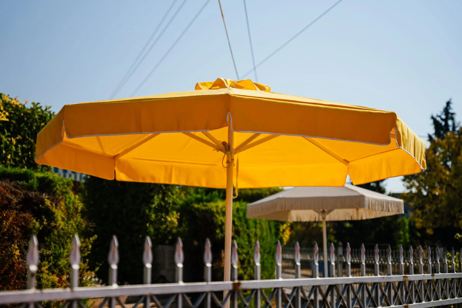 Κίτρινη ομπρέλα Metal Design και λευκή ομπρέλα με κρόσσια στον κήπο της Metal Design στον Βόλο
