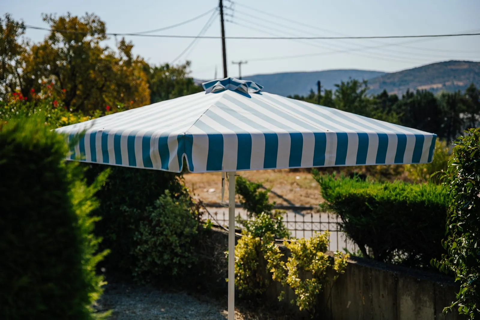 Ομπρέλα Metal Design με λευκό και πετρόλ ριγέ ύφασμα στον κήπο της Metal Design στον Βόλο