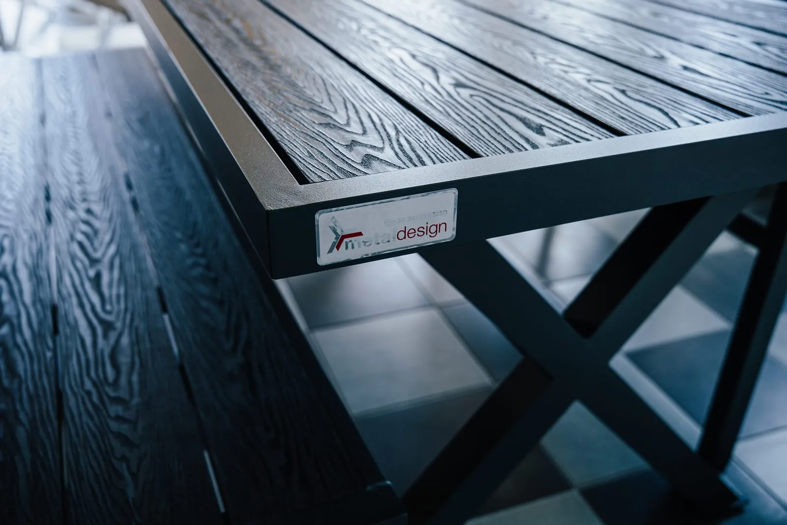 Λεπτομέρεια από τραπέζι Metal Design με σκούρα επιφάνεια με νερά ξύλου και πόδια σε σχήμα Χ